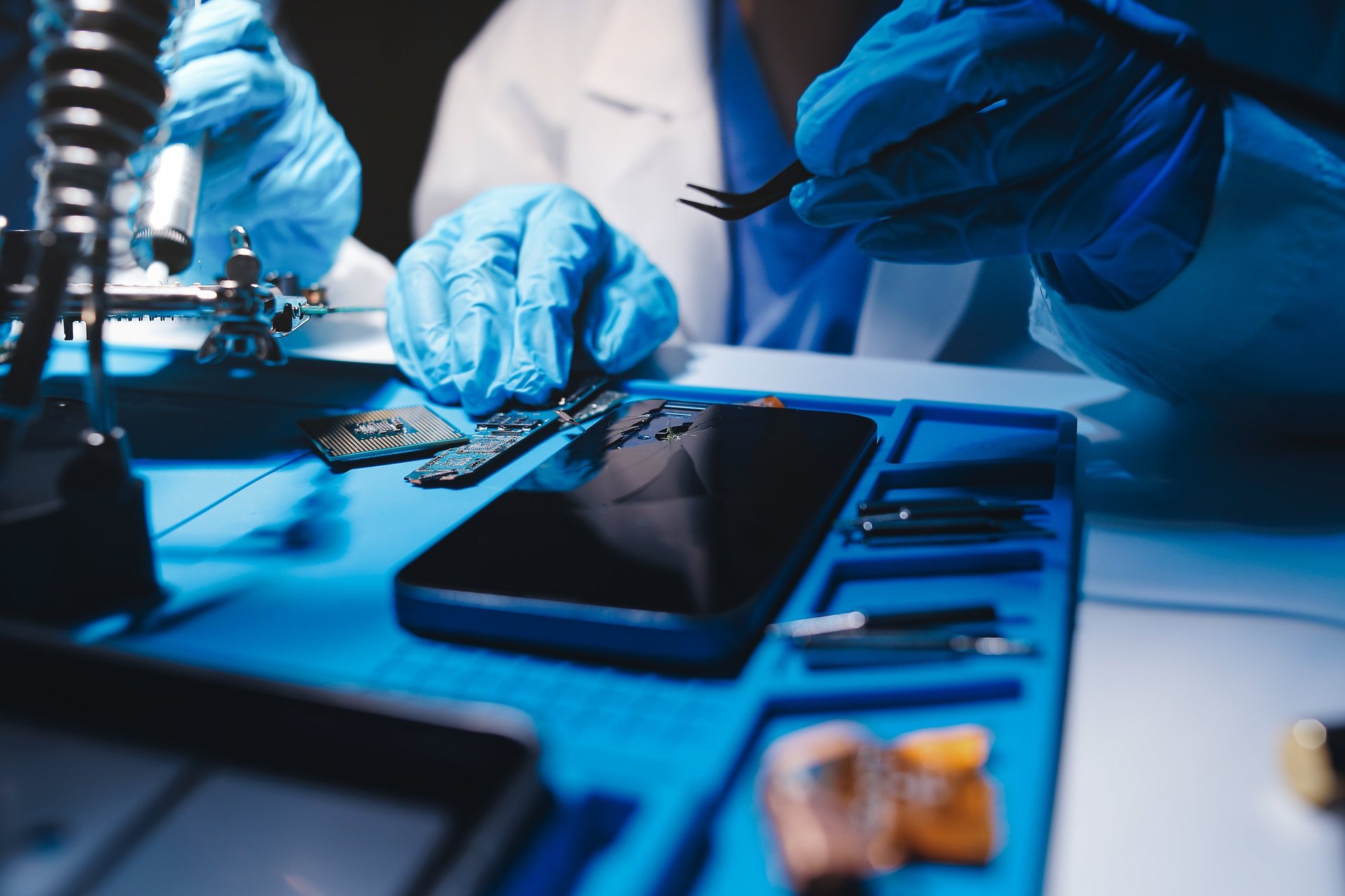 Hands in white gloves carefully repair a broken mobile device